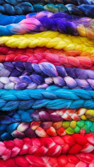 A close-up of Koigu Merino Roving Braid shows thick, soft merino wool yarns in vibrant horizontal rows of yellow, blue, purple, pink, red, and turquoise for a colorful and textured pattern.