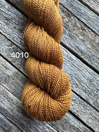 A skein of golden brown Koigu KPM & KPPPM Fingering Weight Yarn, labeled 4010, sits on a weathered wooden surface—ideal for your knitting or crochet projects.