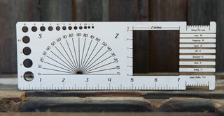 The Apothecary "Almost Everything" Ruler is a wooden multifunctional tool with inch markings, various-sized holes, angle guides, and labeled wire and yarn gauge slots, shown on a stone surface against a wooden background.