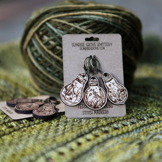 The 💡 Terrarium Light Bulb Progress Keepers 💡 are a set of three wooden knitting markers with plant designs, shown against green yarn and fabric, and attached to a Sunrise Grove Knittery branded card.
