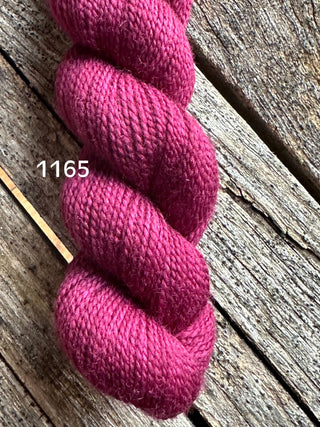 A skein from the KPM and KPPPM Variegated Color Collection, in deep pink shade 1165, rests on a weathered wooden surface, displaying its soft texture—ideal for hand knitting projects.
