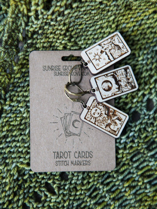 The 🔮 Tarot Card Stitch Markers – The Moon, The Star & The Sun 🔮 set features three tarot-themed stitch markers, ideal as knitting accessories or progress keepers, displayed on a labeled card against textured green knitting.