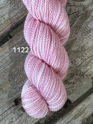 A skein of the KPM and KPPPM Variegated Color Collection, in soft pink with white highlights (color 1122), rests on rustic wood—perfect for your next hand knitting project.