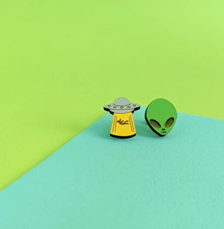 Add a pop of color to your style with the Alien Joyride Earrings—featuring playful green alien heads and yellow UFOs beaming light. Pair them with enamel pins on a green and blue background for an out-of-this-world look!.