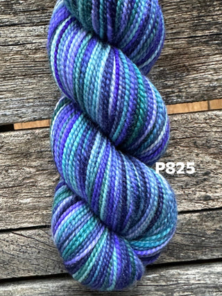 A KPM and KPPPM Variegated Color Collection skein in blue, purple, teal, and white rests on rustic wood. Label P825 appears at the right—ideal for hand knitting projects.
