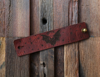 The 🦇 Vampire Bat Under the Moon Shawl Cuff 🦇, with bat and star engravings and a brass accent, rests diagonally on rustic wood, echoing handcrafted charm.