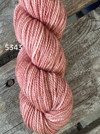 A skein from the KPM and KPPPM Variegated Color Collection in dusty pink (color 5343) rests on a weathered wooden surface—ideal for hand knitting with soft premium merino yarn.