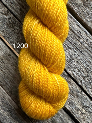 A skein from the KPM and KPPPM Variegated Color Collection rests on weathered wooden planks, with the number 1200 in white text on the left.