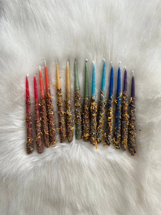 Fourteen Kaleidoscope Beeswax Candles, each in a different vibrant shade, are arranged in a red-to-purple gradient and decorated with dried flower petals on a soft white fur background.