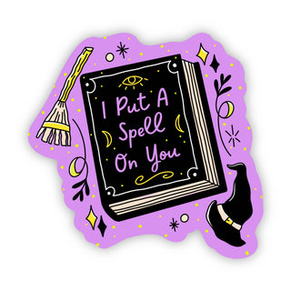 The I Put A Spell On You Sticker features a cute spell book with the phrase on its cover, surrounded by a broom, magic hat, stars, and sparkles on a purple background—perfect as a waterproof vinyl sticker.
