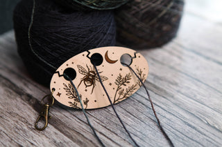 The Yarn Management Tool for Knitters, featuring a charming bee, moon, and leaf design, organizes gray yarn strands as a practical and decorative thread separator. In the background, yarn balls rest on a wooden surface.