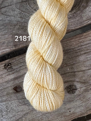A twisted skein of soft, pale yellow KPM and KPPPM Variegated Color Collection yarn labeled 2181 rests on a weathered wooden surface, perfect for hand knitting projects.