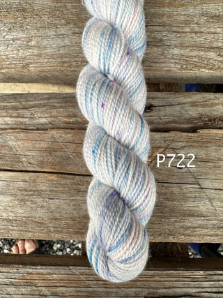 A skein of Bridgerton Collection KPPPM yarn (label P722) with soft pastel speckles in blue, purple, and pink rests on a rustic wooden surface. This premium merino wool offers a luxurious hand-knitting texture.