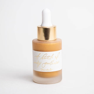 A frosted glass dropper bottle with a gold cap and white label, filled with golden Premium Calligraphy Ink. The handwritten label says A bottle of daily goodness. The bottle is displayed against a plain white background.