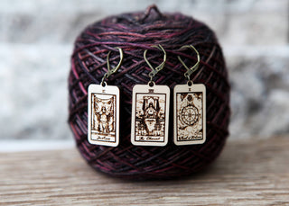 The 🔮 Tarot Card Stitch Markers – Justice, Wheel of Fortune & The Chariot 🔮 are maple wood crochet and knitting accessories with metal hooks, displayed before dark purple yarn as decorative progress keepers.