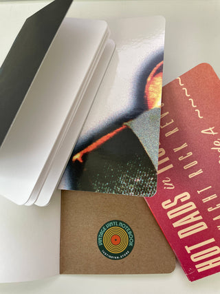 Four pocket-sized notebooks overlap on a white surface: one with blank pages, one with an abstract design, one red with white text, and one Vintage Vinyl Pocket Notebook featuring a colorful circular logo.