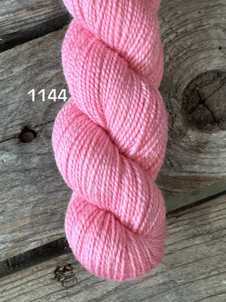 A skein of light pink KPM and KPPPM Variegated Color Collection yarn, color 1144, rests on a rustic wooden surface with visible grain—perfect for hand knitting projects.