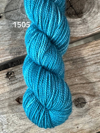 A skein of Koigu KPM & KPPPM Fingering Weight Yarn in bright turquoise blue (color 1505), displayed on a rustic wooden surface with visible knots and grain patterns.