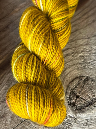 A close-up of a KPM and KPPPM Variegated Color Collection Skein in shade P078—bright yellow with orange and white accents—rests on rustic wood, showcasing its vibrant hues for your next hand knitting project.