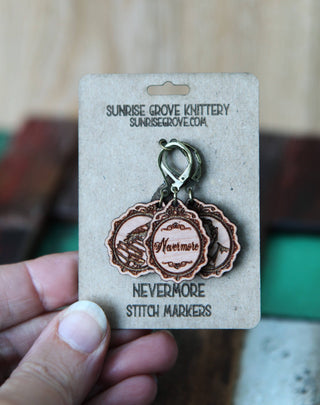 A hand holds a Nevermore Knitting & Crochet Stitch Markers card from Sunrise Grove Knittery, featuring three engraved round wooden stitch markers—an ideal gothic vintage accessory for knitting or crochet.