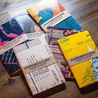 Six Vintage Vinyl Pocket Notebooks with assorted retro covers are displayed on a wooden surface. Each handmade notebook has a brown paper band marked JUSTINKYAW.ORG SECOND COLLECTION.