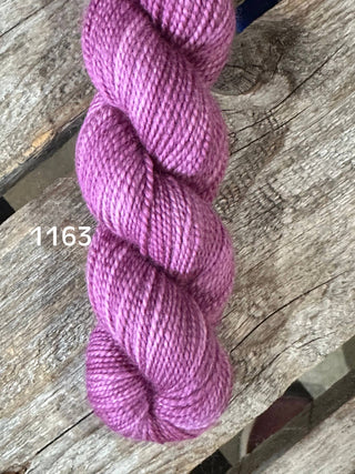 A skein of soft, shiny Koigu KPM and KPPPM Variegated Color Collection yarn in lavender-pink (1163) rests on a rustic wooden surface, perfect for hand knitting.