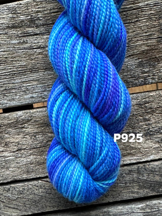 A skein from the KPM and KPPPM Variegated Color Collection rests on a weathered wooden surface, labeled P925—featuring beautiful blue and purple shades perfect for your next hand knitting project.
