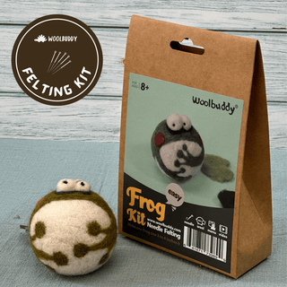 The DIY Needle Felting Kit – Frog is a beginner-friendly kit featuring a cute felt frog. The finished frog appears in front of brown packaging labeled "Frog Kit" and "Woolbuddy," along with an image of the completed project.