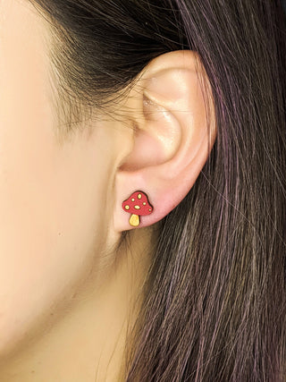 Close-up of a person with straight brown hair featuring a hint of purple wearing Mushroom Earrings, shaped like red and yellow mushrooms and handmade in the USA.