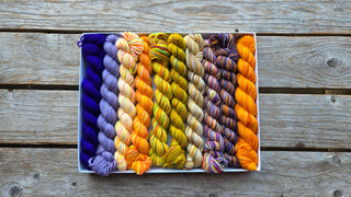 The Spooky Season Koigu Pencil Box showcases eight mini skeins of Merino wool yarn in the Spooky Season colorway, neatly arranged on a wooden surface.