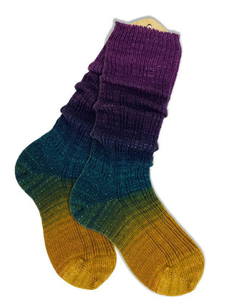 A pair of gradient socks, made with Solemate Sock Yarn in soft merino fingering, shift from mustard yellow at the toes to teal, dark blue, and finish with purple cuffs.