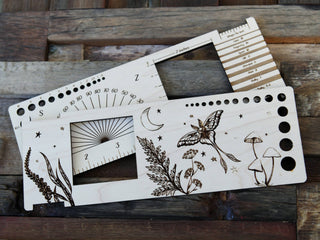 The Luna Moth “Almost Everything” Ruler features ruler markings, hole guides, and nature-themed engravings—moths, plants, mushrooms, and stars—on rustic wood, making it perfect for any fiber arts or crochet ruler collection.