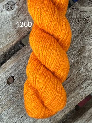 A skein of bright orange KPM and KPPPM Variegated Color Collection yarn, color 1260, sits on a weathered wooden surface—ideal for hand knitting projects.