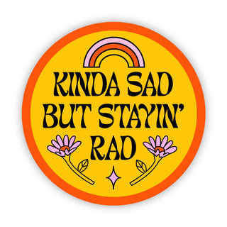 The Kinda Sad But Stayin' Rad sticker is a round, orange-bordered vinyl badge with a yellow background, rainbow, pink flowers, and bold black text. It’s waterproof and weather-resistant for lasting style.