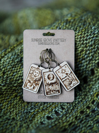🔮 Tarot Card Stitch Markers – The Moon, The Star & The Sun 🔮 by Sunrise Grove Knittery feature intricate wood-burned designs, displayed on a branded card atop green knit fabric—unique knitting accessories perfect as progress keepers for your next project.