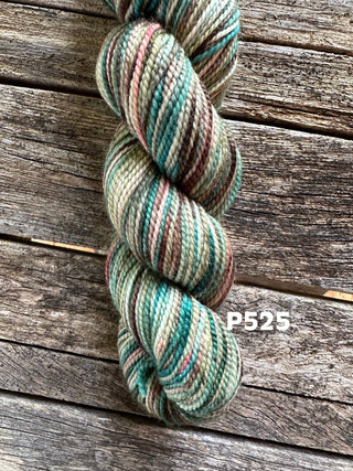 A skein from the KPM and KPPPM Variegated Color Collection in green, brown, and beige (code P525) rests on a weathered wooden surface—ideal for hand knitting projects.