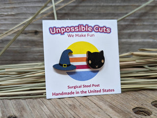 The Witch Hat & Cat Earrings are shown on a branded Unpossible Cuts card, set against straw and rustic wood—perfect for pairing with your favorite Halloween accessories.