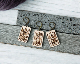 Three maple wood stitch markers—The Tower, The Devil & Judgement tarot cards—feature engraved designs and gold hooks, displayed on a gray textured surface. Perfect for fans of tarot crochet accessories.
