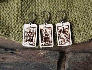Three wooden Tarot Card Stitch Markers—The High Priestess, The Empress, and The Emperor—lie on textured green knit fabric, highlighting their charm for knitting or crochet enthusiasts.