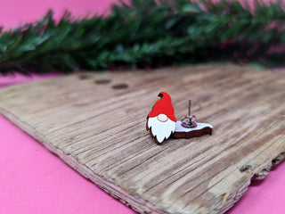 The 🍄 Gnome Earrings 🍄 feature a charming gnome shape with a red hat and white beard, displayed on a wooden board with festive decor—perfect for fans of handmade jewelry and unique accessories.