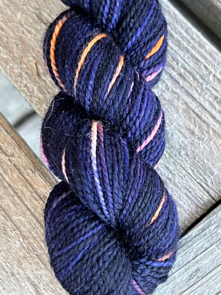 A skein from the KPM and KPPPM Variegated Color Collection, featuring vibrant orange, purple, and pink tones, rests on a weathered wooden surface—ideal for hand knitting projects.