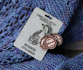 Nevermore Knitting & Crochet Stitch Markers—wooden Poe-inspired markers on a raven-illustrated card, displayed atop purple-blue knit fabric. Perfect gothic knitting accessories for literary lovers.