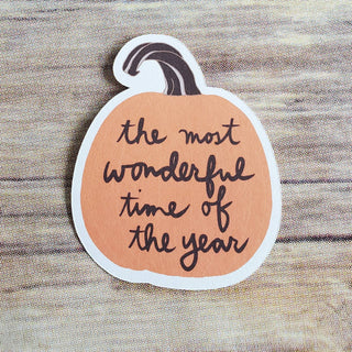 The Most Wonderful Time of the Year Pumpkin Sticker is an eco-friendly paper sticker with a pumpkin shape and cursive text, shown on a wooden surface.