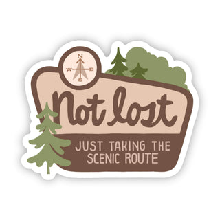 The Not Lost, Just Taking The Scenic Route | Sticker is a waterproof vinyl sticker featuring trees, a compass, and cheerful brown text—great for promoting mental health awareness on all your adventures.