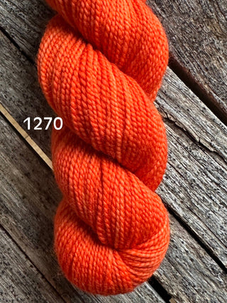 A skein from the KPM and KPPPM Variegated Color Collection in bright orange (color 1270) rests on a rustic wooden surface—perfect for your next hand knitting project.