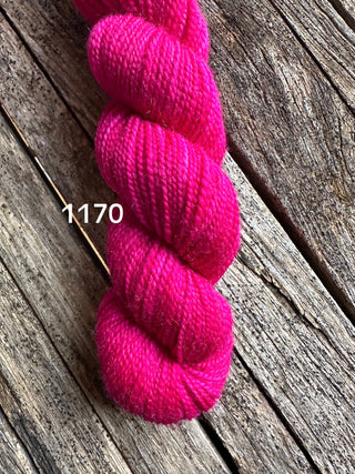 A skein from the KPM and KPPPM Variegated Color Collection in bright pink (1170) rests on rustic wood, ideal for hand knitting projects.