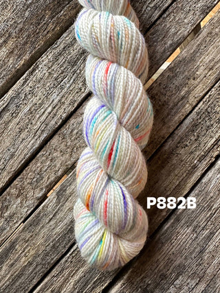 A skein from the KPM and KPPPM Variegated Color Collection, in a light shade with multicolored specks, ideal for hand knitting, is placed on a rustic wooden surface. "P882B" is visible on the right side of the image.