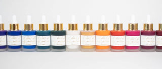 Twelve bottles of Premium Calligraphy Ink with gold caps and white labels, filled with vibrant colors, are arranged in a row against a plain white background.