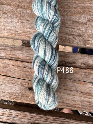 A skein of Bridgerton Collection KPPPM yarn in light blue, white, and gray sits on a weathered wooden surface. The label P488 is shown, making it ideal for hand knitting projects with this premium merino wool yarn.