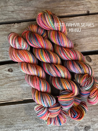 Three skeins of KIHNU-color Merino wool from the Eesti Rahva (Estonian Folk) Series 2025 - KPPPM rest on a rustic wooden surface. Their vibrant hues evoke traditional Estonian handicrafts. Text reads: EESTI RAHVA SERIES KIHNU.